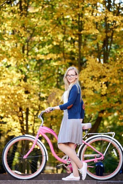 Chica atractiva de pelo largo rubia atractiva con asas de bicicleta rosa moderna