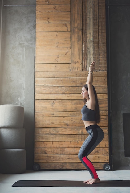 Chica atractiva practicando yoga. Mujer joven haciendo asana pose incómoda en la estera en el interior del club deportivo, espacio de copia