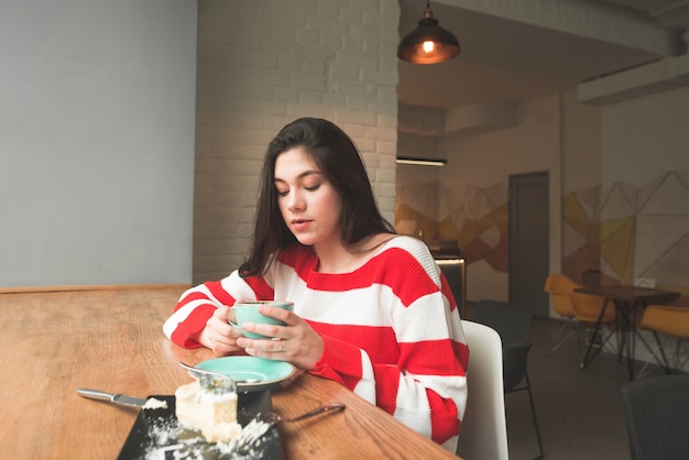 Foto chica atractiva en ropa casual sentado en un café en la ventana con una taza de café