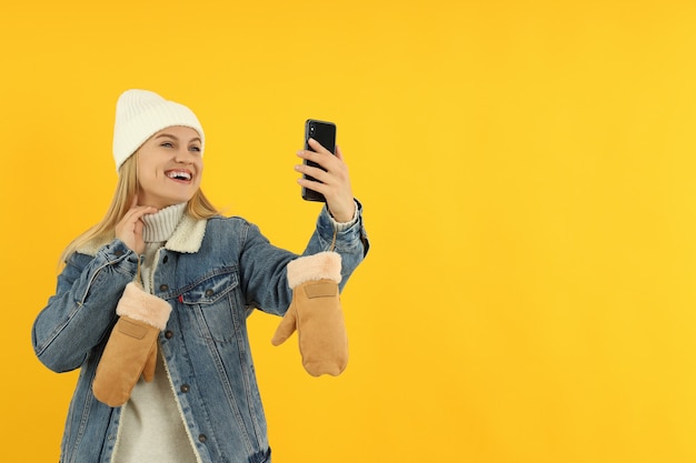 Chica atractiva en ropa de invierno tomar un selfie sobre fondo amarillo