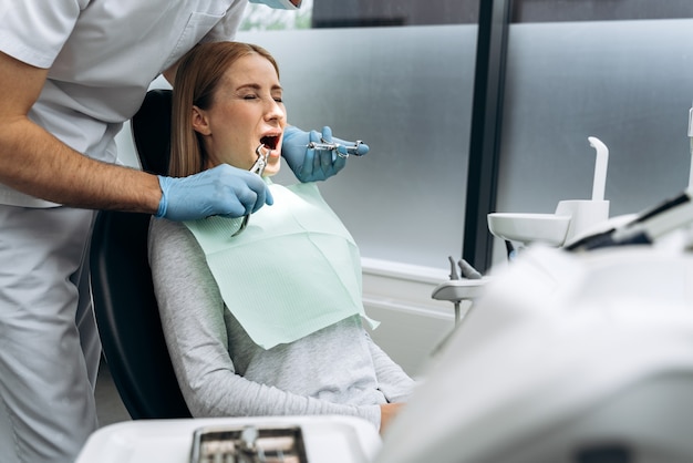 Chica atractiva en un sillón dental con los ojos cerrados y la boca abierta. La mujer tiene miedo de tratar los dientes