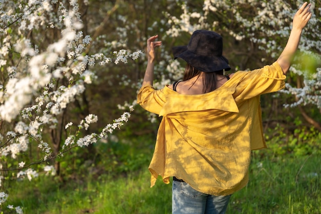 Foto una chica atractiva con un sombrero entre árboles en flor disfruta del olor de las flores de primavera