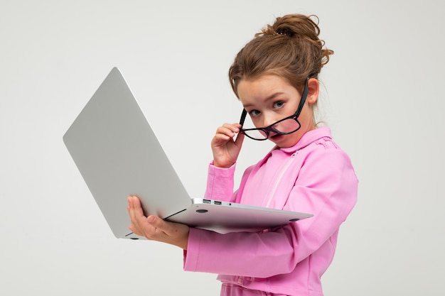 Chica atractiva sorprendida en un traje rosa lee las noticias en una computadora portátil sobre un fondo blanco de estudio