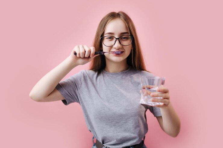 Chica atractiva sosteniendo un vaso con agua y cepillando los dientes