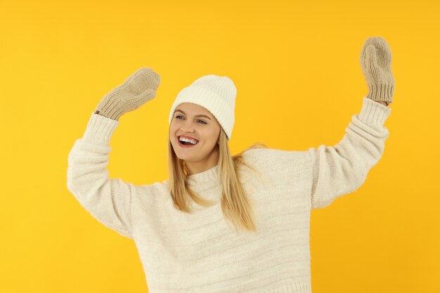 Chica atractiva en suéter, gorro de punto y guantes sobre fondo amarillo.