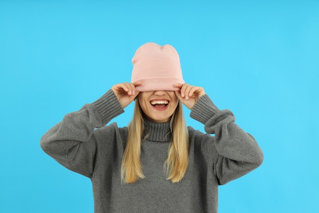 Chica atractiva en suéter y gorro de punto sobre fondo azul.