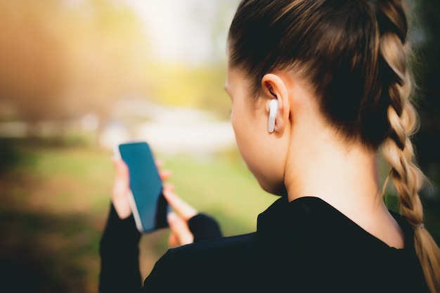 Chica atractiva usando su teléfono, auriculares inalámbricos mientras se ejecuta en el parque