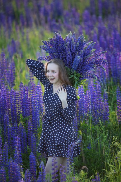 Chica atractiva con un vestido largo morado en un campo con altramuces.