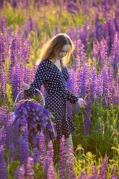 Chica atractiva con un vestido largo morado en un campo con altramuces.