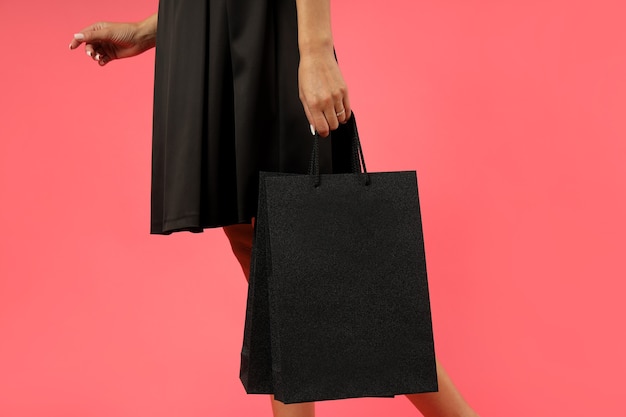 Chica atractiva en vestido negro con bolsas de papel sobre fondo rosa.