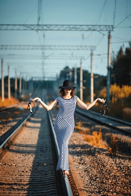 Chica atractiva con un vestido de rayas está caminando sobre el ferrocarril