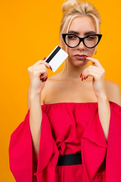 Chica atractiva con un vestido rojo tiene una tarjeta de crédito con un diseño para el banco en un espacio amarillo