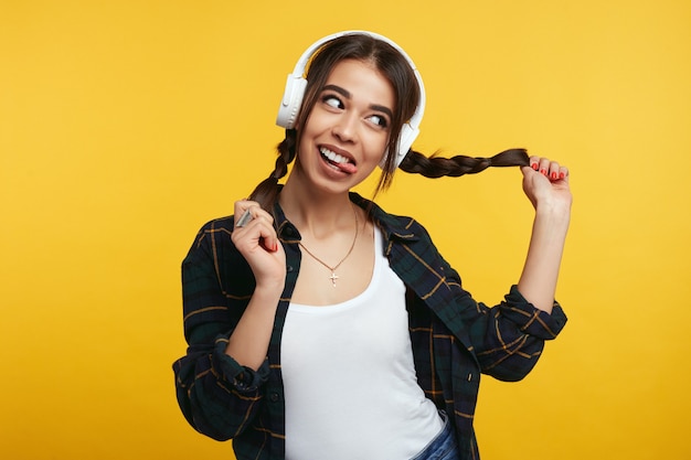 Chica con auriculares blancos juega con sus colas de caballo y saca la lengua