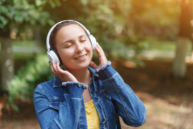 Chica con auriculares caminando en el parque en un día soleado y escuchando música