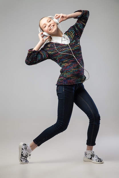 Chica con auriculares cantando y bailando inclinándose hacia atrás. Sobre fondo gris. Retrato de cuerpo entero.