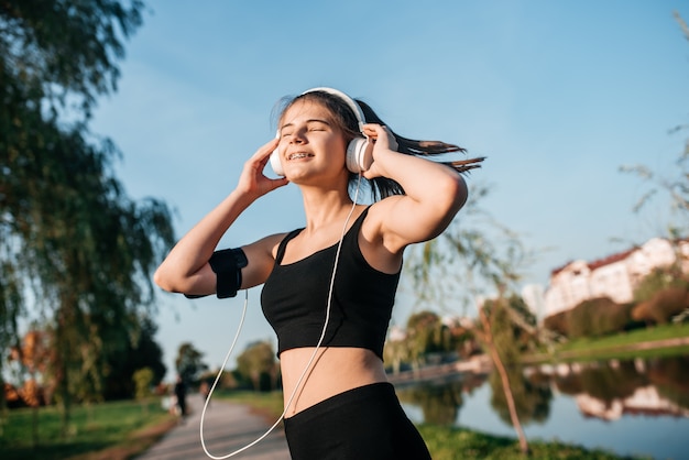 Una chica con auriculares se dedica a hacer ejercicio al aire libre en una metrópoli. correr y deportes en verano