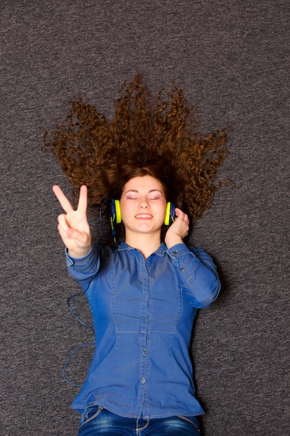 Foto chica en auriculares disfrutando de la música mientras se está acostado en una alfombra