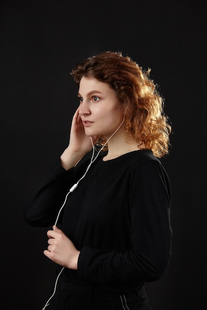 Chica con auriculares escucha música. Retrato de primer plano sobre un fondo negro.