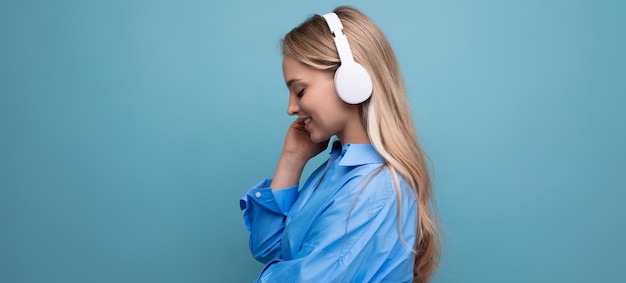 Una chica con auriculares inalámbricos grandes disfruta y se relaja con la música de la aplicación en un azul