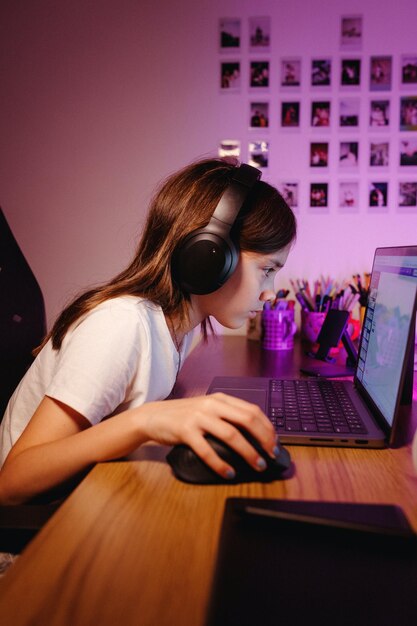 Una chica con auriculares y jugando en una computadora portátil Foto