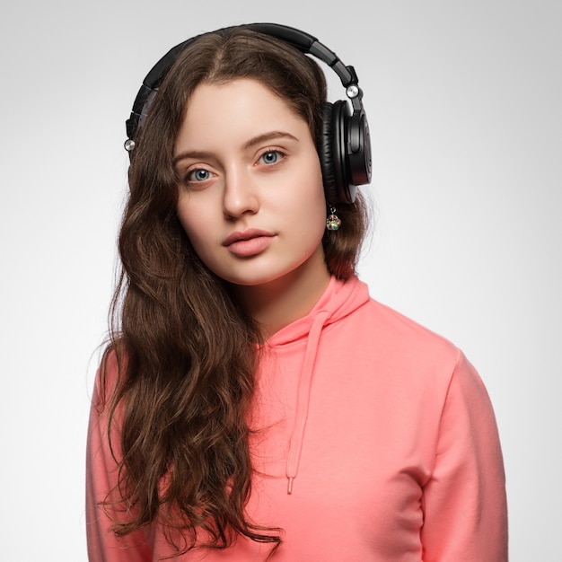 Chica en auriculares con pelo largo sobre un fondo claro en ropa rosa.
