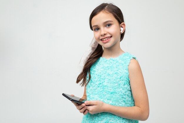 Chica con auriculares en sus oídos y un teléfono en sus manos en una pared blanca con espacio en blanco