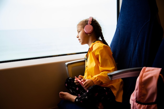 Una chica con auriculares en un tren mira por la ventana. Viaje.