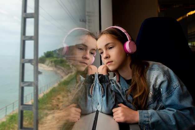 Una chica con auriculares en un tren mira por la ventana