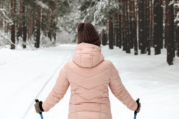 Una chica auténtica con una chaqueta rosa posa para la cámara con bastones de esquí o marcha nórdica