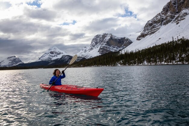 Chica aventurera en kayak en un lago glaciar rodeado por las Montañas Rocosas canadienses