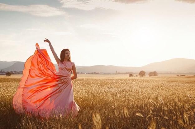 Chica bailando en un campo con un hermoso vestido rosa al atardecer