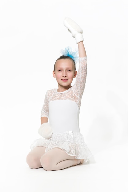Chica bailarina en falda de tutú de ballet blanco sentada sobre fondo blanco