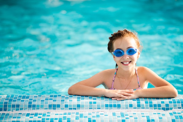 La chica se baña en la piscina con gafas azules para nadar.