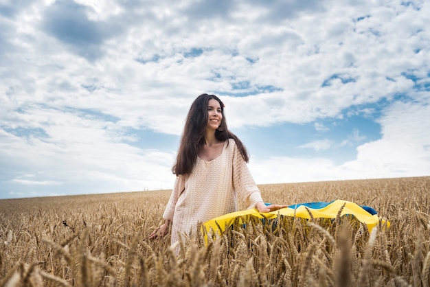 Chica con bandera de Ucrania y camina por un campo de trigo maduro. Paz en Ucrania. Disfruta el estilo de vida
