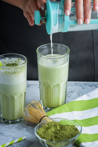 La chica barista agrega leche al vaso. Una bebida saludable latte té verde matcha. Foto recortada de cerca