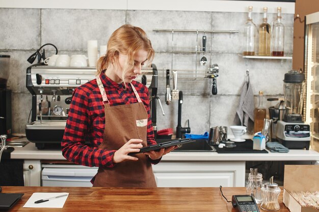 Chica Barista trabajando en la cafetería mantiene la tableta en sus manos