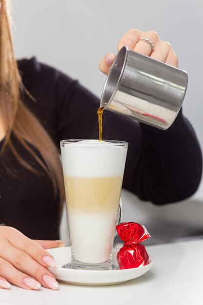 Chica barista vierte leche de una jarra de leche de metal en un vaso de café