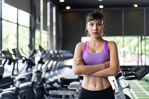 Chica bastante asiática con seis paquetes de ropa deportiva de color púrpura de pie y cruzando los brazos en el gimnasio o gimnasio.