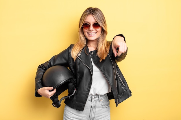 Chica bastante rubia apuntando a la cámara eligiéndote. concepto de casco de moto