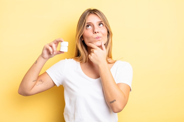 Chica bastante rubia pensando, sintiéndose dudoso y confundido. concepto de botella de pastillas