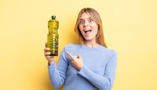 Chica bastante rubia que parece emocionada y sorprendida apuntando hacia un lado. concepto de aceite de oliva