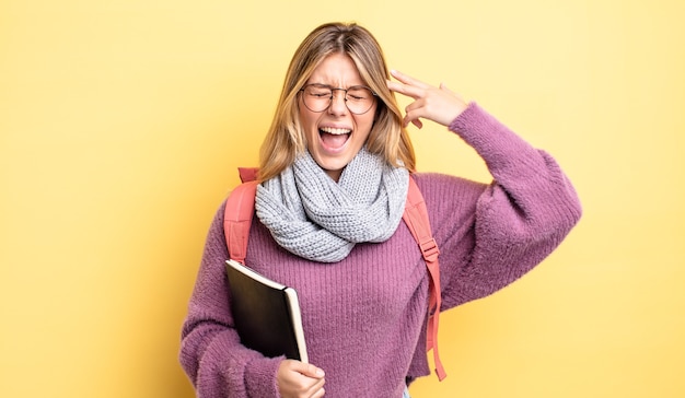 Chica bastante rubia que parece infeliz y estresada, gesto de suicidio haciendo signo de pistola. concepto de estudiante