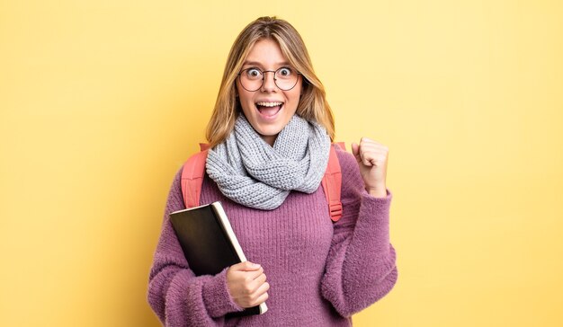 Chica bastante rubia sintiéndose conmocionada, riendo y celebrando el éxito. concepto de estudiante