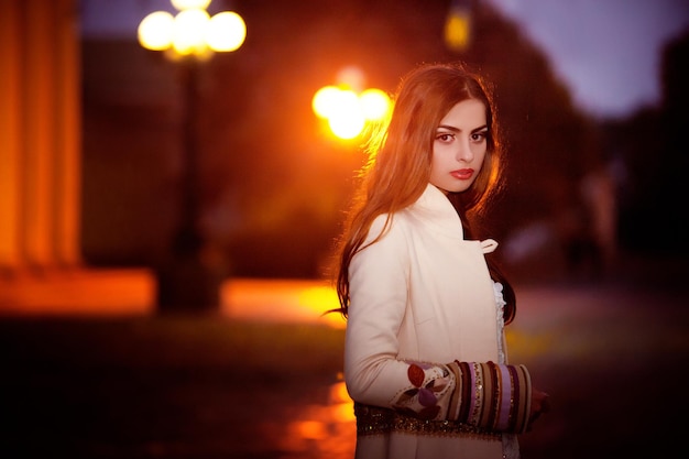 Una chica con bata blanca se para en la calle por la noche.