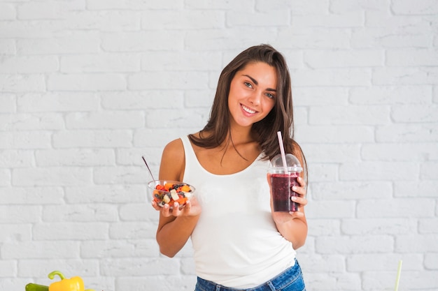 Foto chica con batidos en taza de plástico y ensalada de frutas en sus manos