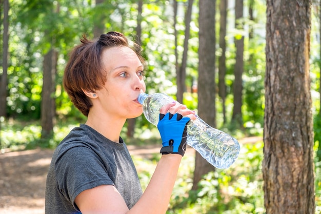 Chica bebe agua de una botella mientras entrena en el parque