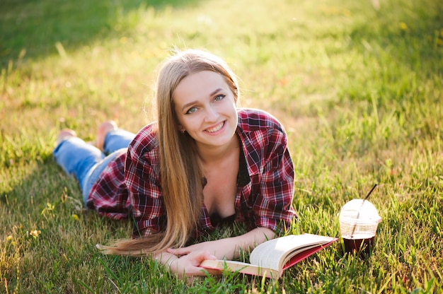 Foto chica beber jugo y leer un libro en un parque.