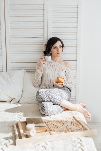 Chica bebiendo café y un cruasán en la cama