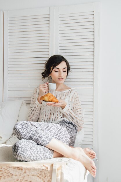 Chica bebiendo café y un cruasán en la cama