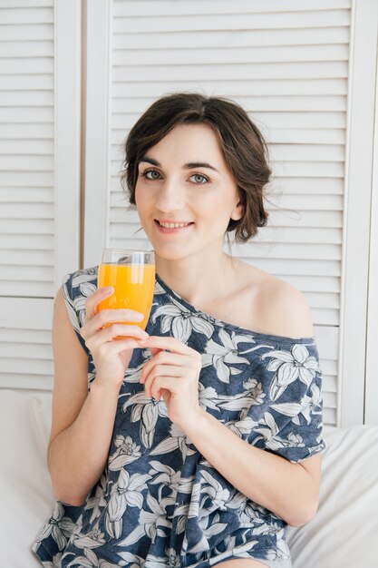 Chica bebiendo jugo de naranja en el desayuno en la cama